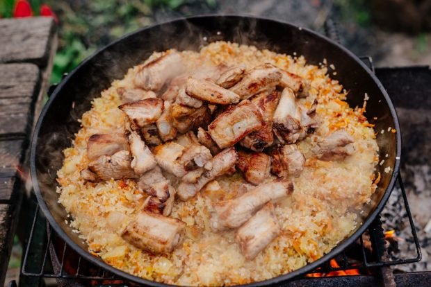 Pilaf of pork ribs in a cauldron on a campfire 